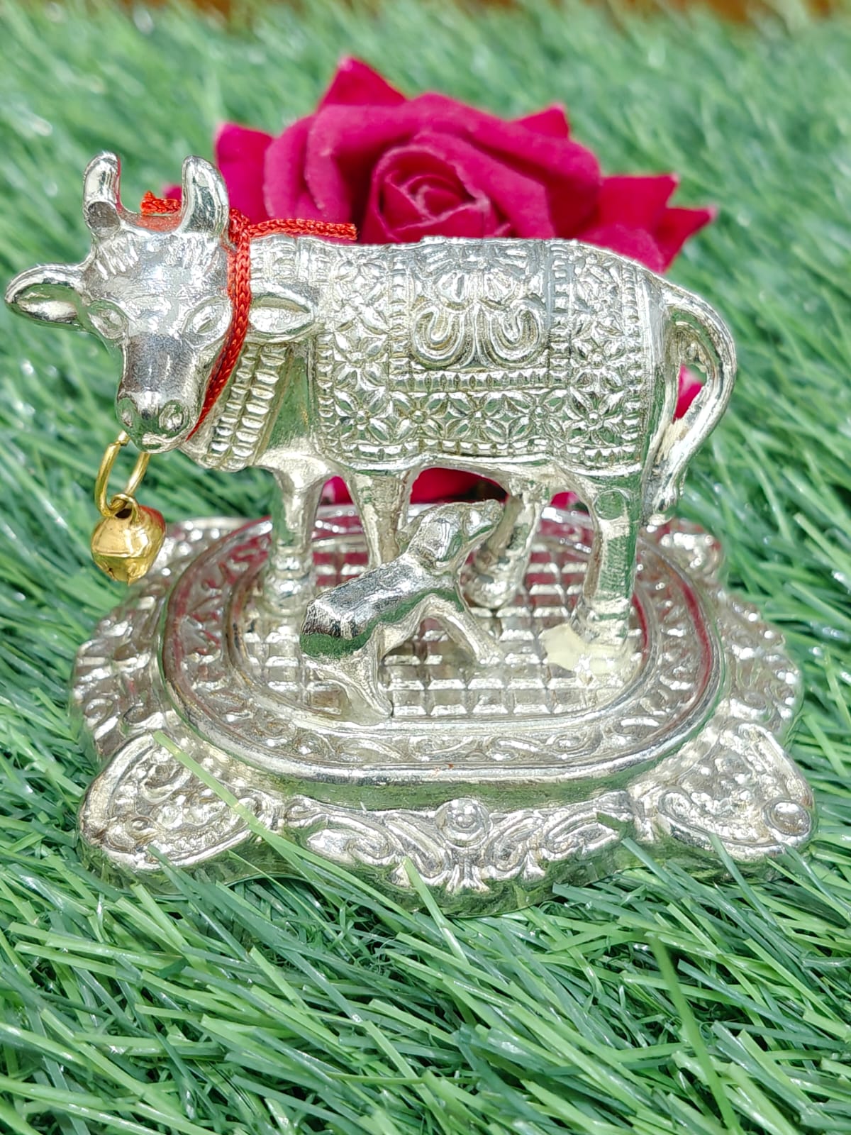 Silver cow and calf statue with a bell on a green grass background