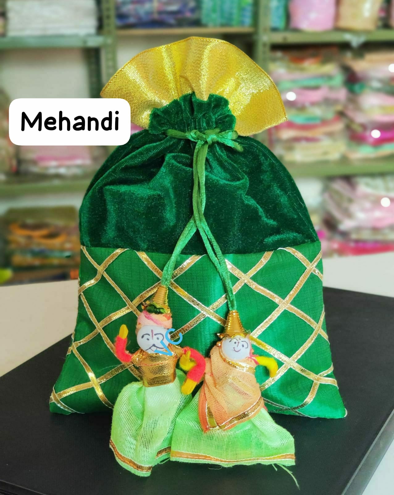 Green decorative bag with embroidered designs on a black surface, labeled 'Mehandi'.