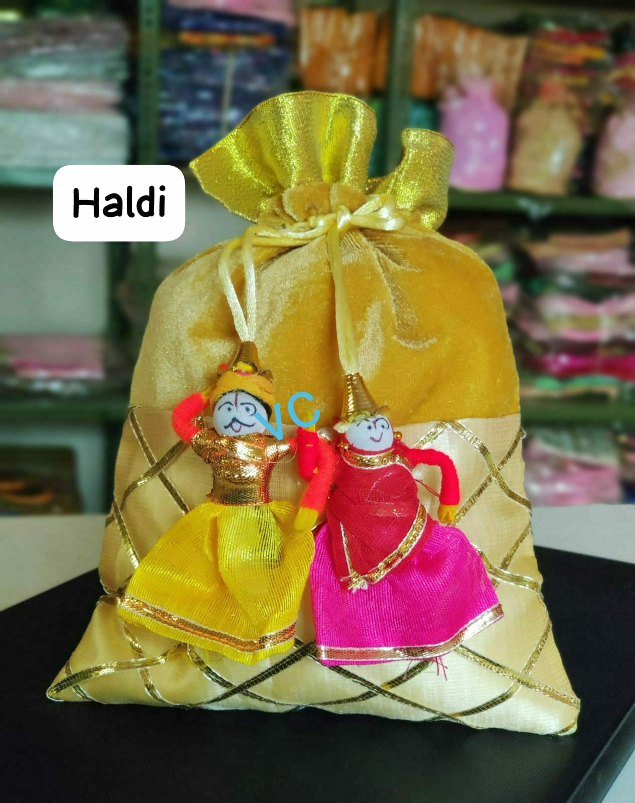 Decorative haldi bag with two small dolls on a black surface, with 'Haldi' text label.