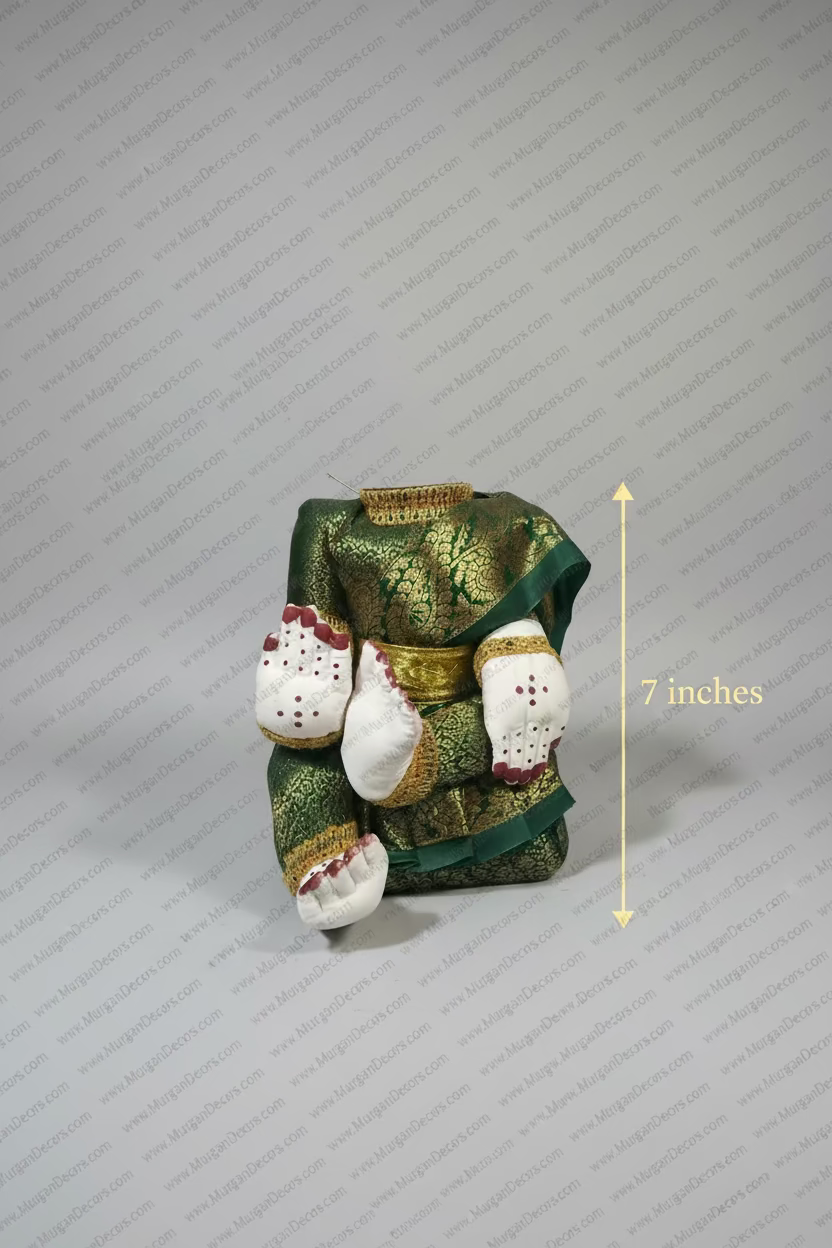 Shop Varalakshmi amman Idol body with Purple silk saree for Decoration in USA at MuruganDecors . A traditional Thai doll dressed in a green and gold brocade robe with white hands and feet decorated with red dots, sitting on a white plastic surface.