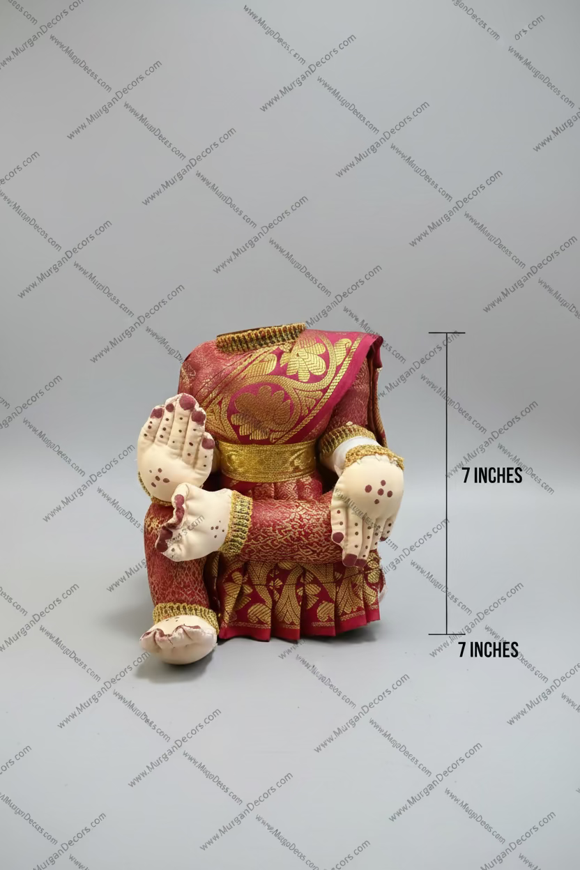 A decorative figurine of a seated figure wearing a richly patterned magenta and gold traditional outfit, with cream-colored hands and feet, displayed on a dark wooden surface.