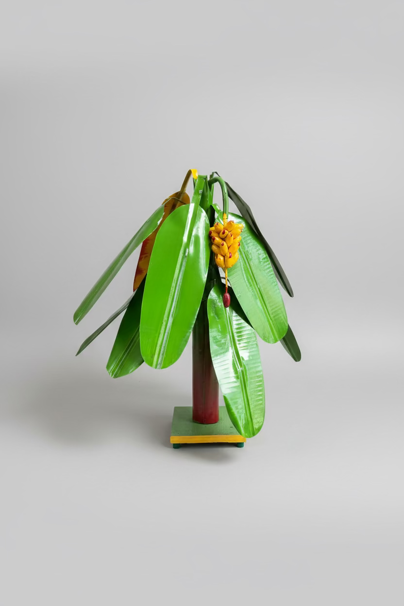 A decorative metal sculpture of a banana plant with glossy green leaves and a yellow banana flower cluster, mounted on a small pedestal.